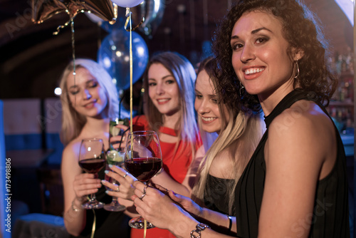 Cheerful girls clinking glasses of wine at the party in night club