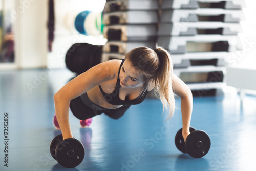 Fototapeta Naklejka Na Ścianę i Meble -  Young strong girl doing push-ups on dumbbells in the gym