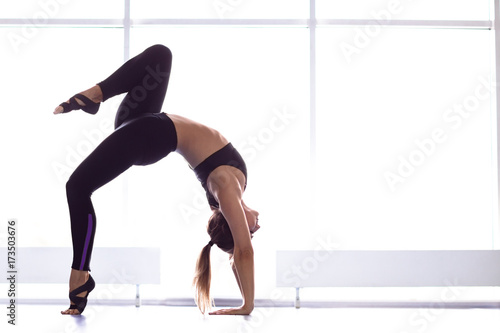 Young attractive woman practicing yoga near window. Chakrasana