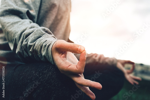 Close up of female hands in meditation pose and practicing yoga in urban park at sunset. Blurred background, flares and sunlight