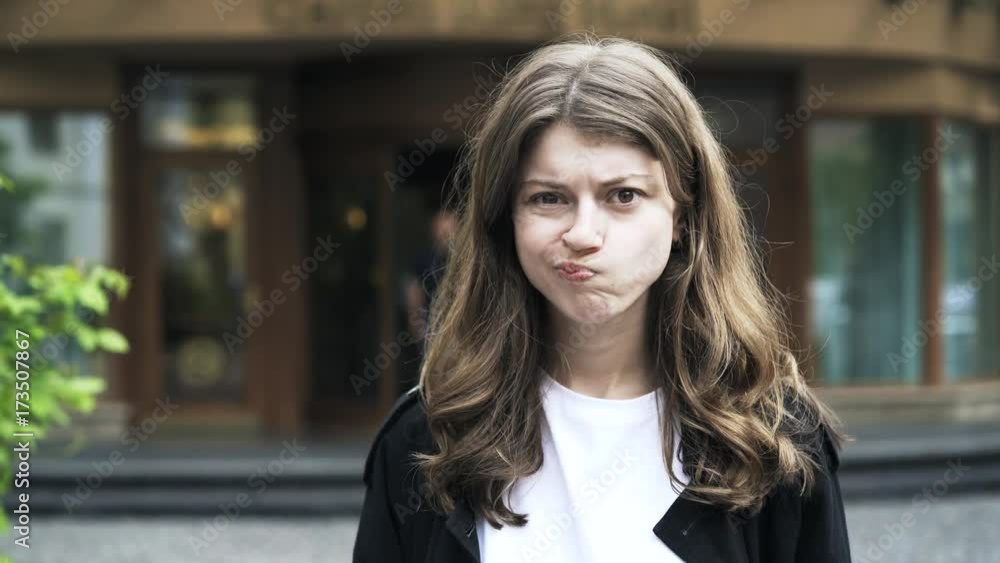 Close up of a beautiful young woman with long brown hair looking at the viewer, sticking out her tongue and making funny faces while standing in the street. Handheld real time close up shot Close up of a beautiful young woman with long brown hair looking at the viewer, sticking out her tongue and making funny faces while standing in the street. Handheld real time close up shot