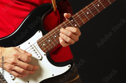 Musician put fingers for chords on electric guitar on the black background