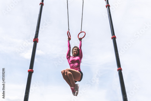 Cute sporty girl training on rings outdoor