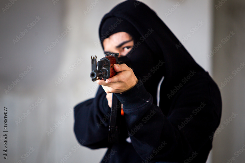 Unidentified man in black suit with face masked is aiming assault rifle to the target close up. Unidentified man in black suit with face masked is aiming assault rifle to the target close up.