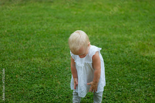 Cute blond lond baby girl playing on the grass in a park photo