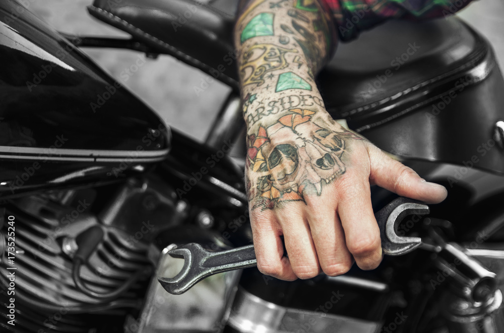 Fototapeta premium Wytatuowany klucz trzymający rękę obok silnika motocykla. Custom shop dla koncepcji rowerów