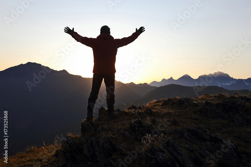 tourist with arms raised standing on the mountain at dawn