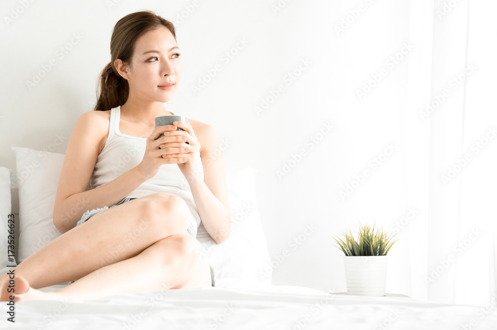 Asian beauty woman wake up and drinking coffee on white bed in white bedroom in morning Asian beauty woman wake up and drinking coffee on white bed in white bedroom in morning