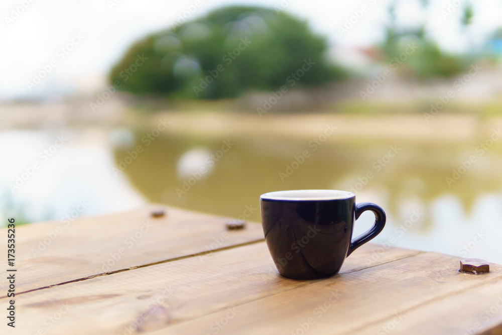 espresso or ristretto coffee in dark blue cup on the wooden table near the river in sunny day.