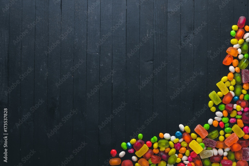 Fototapeta premium Colored candies, sweets and lollipops. On a black wooden background. Top view. Free space.