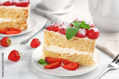 Slice of delicious cake decorated with strawberries and mint on plate