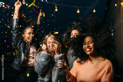 Group of female friends enjoying night party, throwing confetti