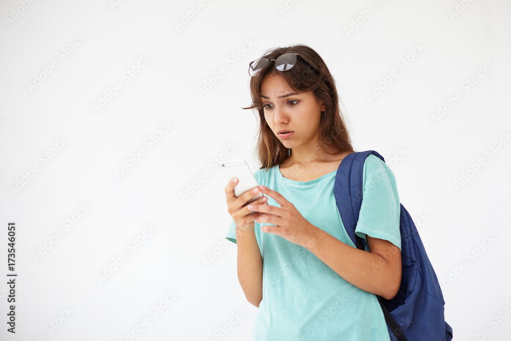 Cute schoolgirl with dark hair wearing oversize t-shirt and eyeglasses on head holding cell phone, messaging online, typing text message, having thoughtful concentrated expression on her face Cute schoolgirl with dark hair wearing oversize t-shirt and eyeglasses on head holding cell phone, messaging online, typing text message, having thoughtful concentrated expression on her face