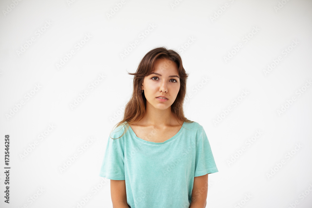 Isolated portrait of teenage girl of Hispanic appearance wearing oversize top looking at camera with serious or pensive expression on her face. Sad ot thoughtful brunette young woman posing indoors Isolated portrait of teenage girl of Hispanic appearance wearing oversize top looking at camera with serious or pensive expression on her face. Sad ot thoughtful brunette young woman posing indoors