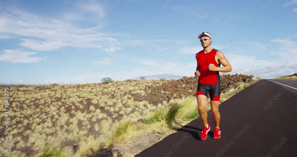 Runner man running in triathlon suit training for Iron man on Hawaii. Fit male triathlete exercising on road in beautiful nature on Big Island, Hawaii. Runner man running in triathlon suit training for Iron man on Hawaii. Fit male triathlete exercising on road in beautiful nature on Big Island, Hawaii.