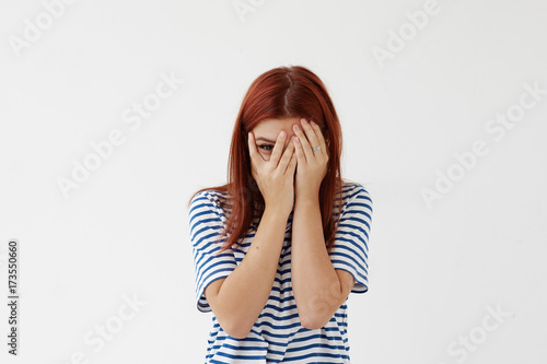 Quadro su tela Picture of shy timid teenage girl with colored hair covering face with hands and peeping through her fingers at camera