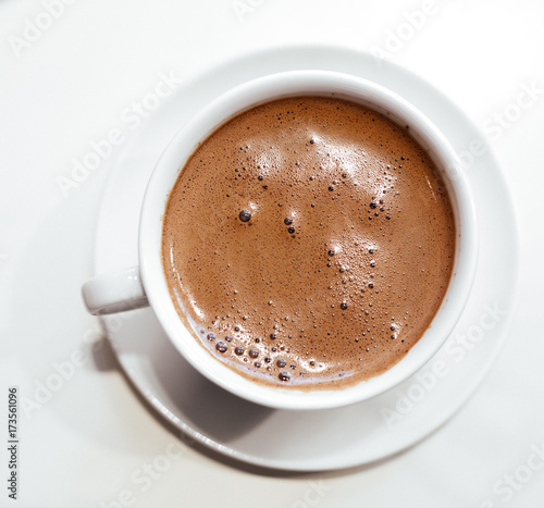 Cappuccino or hot chocolate with frothy foam, white coffee cup top view closeup isolated on white background.