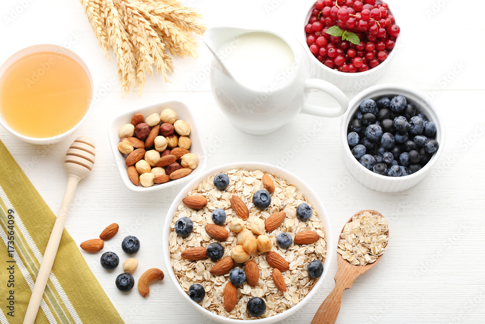 Oat flakes with berries, honey, milk and nuts on wooden table Oat flakes with berries, honey, milk and nuts on wooden table