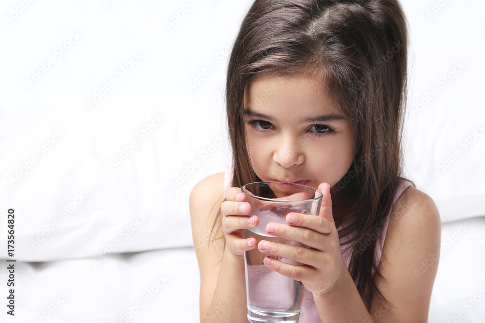 Beautiful little girl drinking water on white bed Beautiful little girl drinking water on white bed