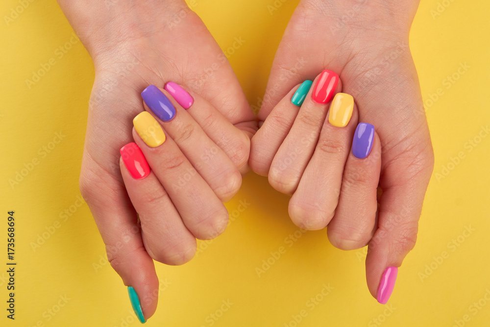 Fototapeta premium Female nails varnished in different colors. Womans nails covered with multicolor polish on yellow background, top view.