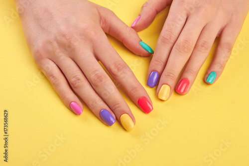 Female well-groomed hands with manicure. Young girl hands polished with different colors nail on yellow wooden background.