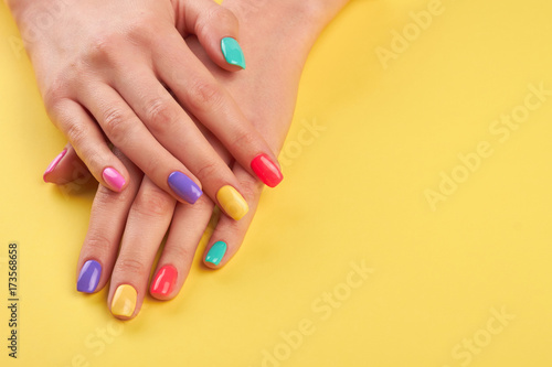 Female hands with summer manicure. Teen girl hands with bright summer manicure on yellow background, copy space.