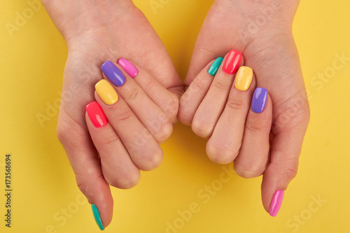 Female nails varnished in different colors. Womans nails covered with multicolor polish on yellow background  top view.