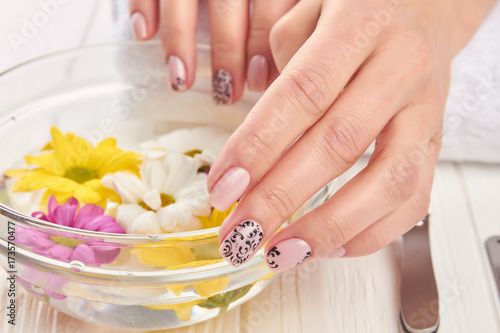 Spa treatment for female hands. Young woman beautiful hands in glass bowl with water and floating chrysanthemums. Hands treatment and nails care.