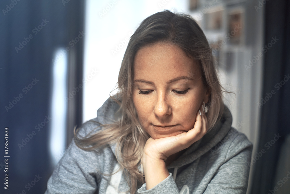 Pensive woman at home, sitting on chair, looking down and laying her head on arm Pensive woman at home, sitting on chair, looking down and laying her head on arm