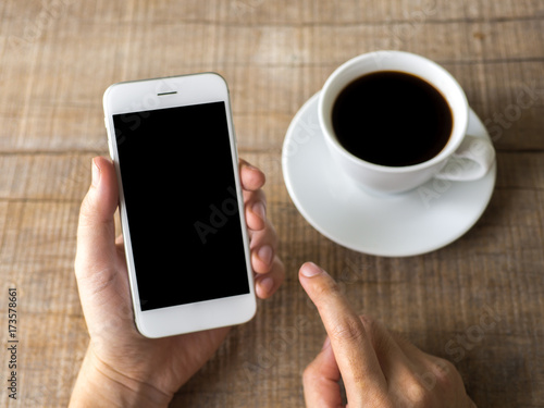 Close up business man's hand holds smart phone with black isolated screen over background of notebook, coffee on wooden background