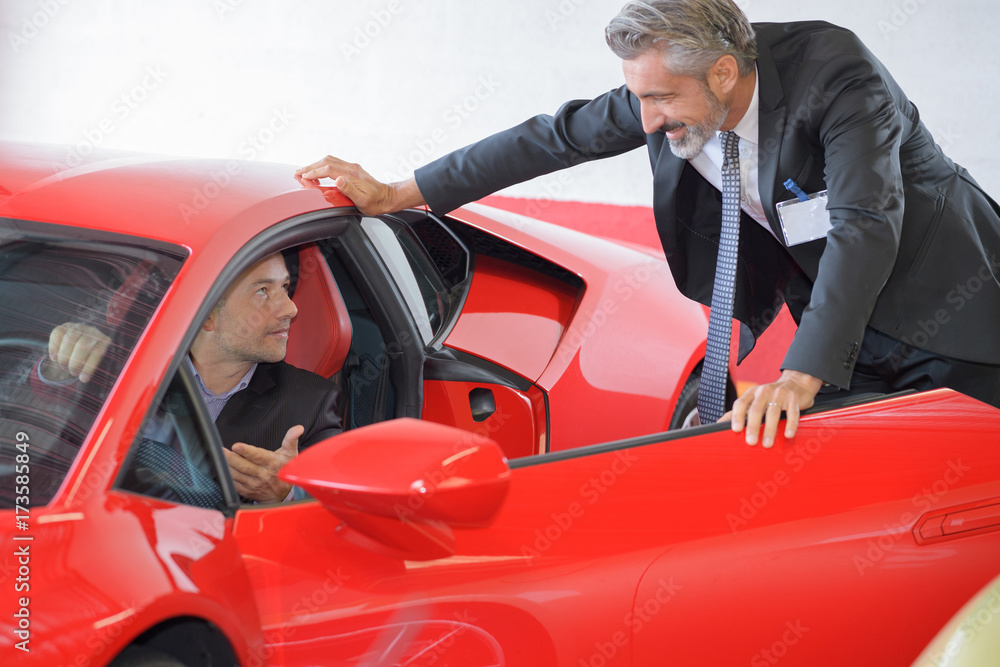 businessman with car dealer buying a new red sport car