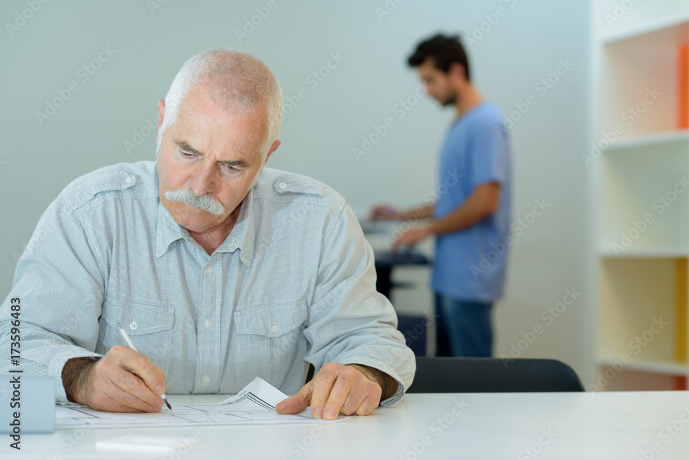 calm senior man writing on paper in library calm senior man writing on paper in library