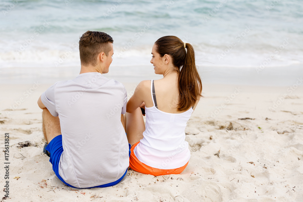 Young couple looking at each other while sitting on beach Young couple looking at each other while sitting on beach