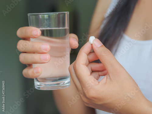 Closeup woman hand with pills medicine tablets and glass of water in her hands. Healthcare, medical supplements concept