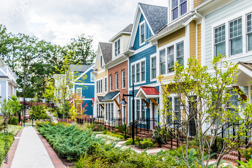 Row of colorful, red, yellow, blue, white, green painted residential townhouses, homes, houses with brick patio gardens in summer photo