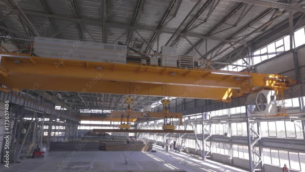 Yellow overhead crane with electromagnetic beam grippers carries steel cargo in engineering plant shop warehouse. Yellow overhead crane with electromagnetic beam grippers carries steel cargo in engineering plant shop warehouse.
