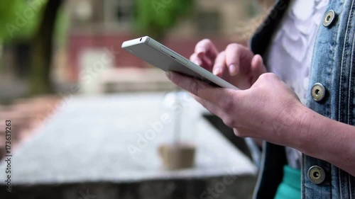 A woman with a mobile phone at a city fountain. A young woman is typing a message on her smartphone. Almaty. Kazakhstan.
