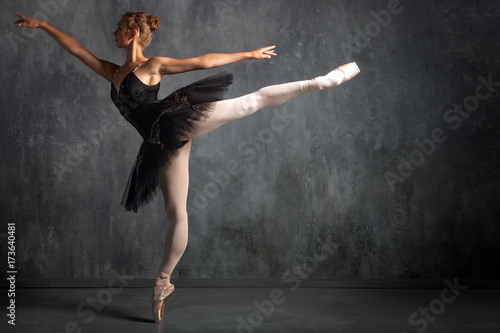 Beautiful attractive blonde woman primer ballerina in a black dance pack, white pantyhose and pointe shoes beautifully dances ballet in a dark studio
