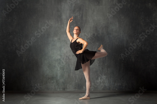 Beautiful attractive blonde woman baterina in a black dance tutu, white pantyhose and pointe shoes beautifully dances ballet in a dark studio