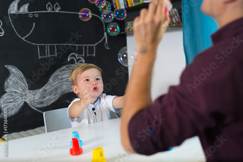 Cute little playfull toddler boy amazed by milky bubbles at child therapy session. Private one on one homeschooling with didactic aids.