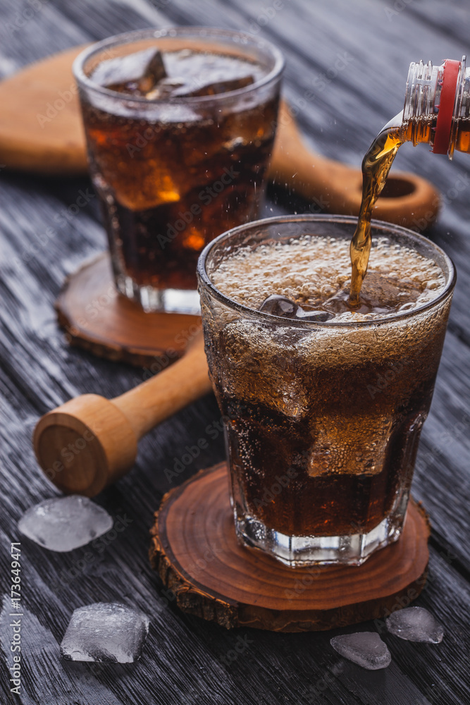 cola with ice in a glass on a black wooden table. cola with ice in a glass on a black wooden table.