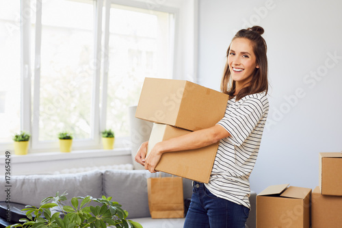 Obraz na plátně Young woman moving into new apartment holding cardboard boxes with belongings