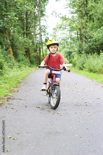 Child boy on a bicycle on bicycle path in summer. Boy cycling outdoors in safety helmet
