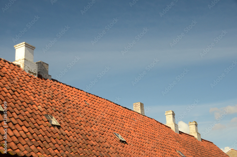 Red tile roof with white chimneys seen with a blue sky as background.