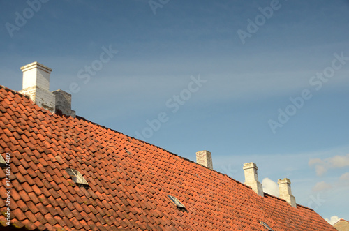 Red tile roof with white chimneys seen with a blue sky as background. © Kim