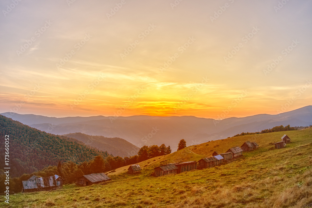 Beautiful sunset on a blue sky background. On the slope of the mountain there are small wooden houses.