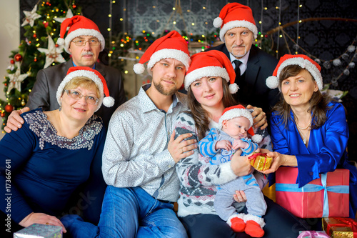 a big happy family in caps of Santaclaus celebrates Christmas, gives each other presents and has fun