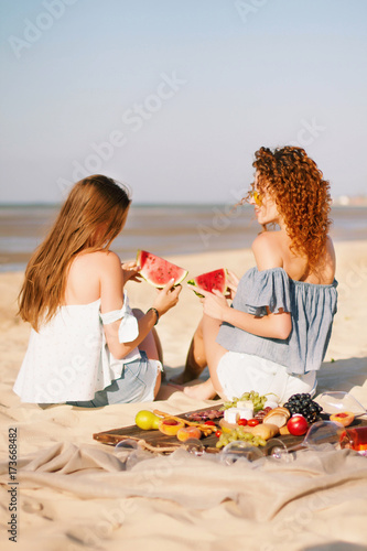 Two young female friends  on the sea shore enjoying  with watermelon.