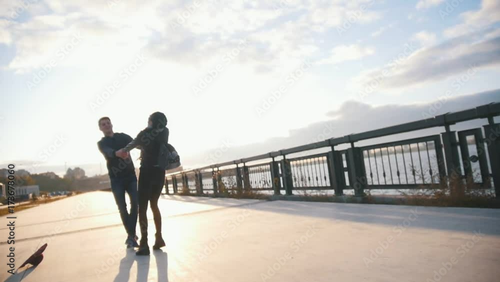 Young couple on the city promenade, man hug and spin girlfriend at sunset, slow-motion Young couple on the city promenade, man hug and spin girlfriend at sunset, slow-motion