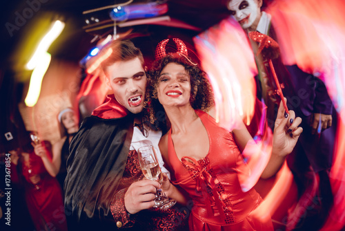 Long exposure. Motion blur. A guy dressed as a vampire and a girl dressed as a demon posing with champagne glasses.